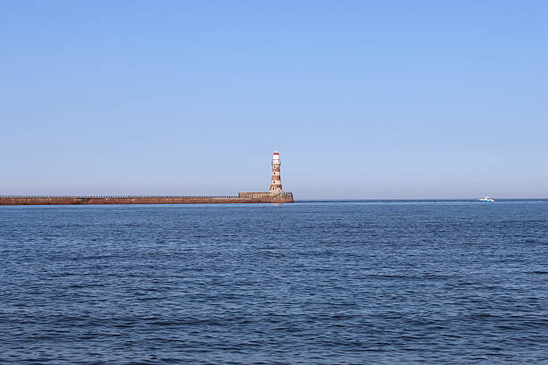 view of Chania’s Venetian lighthouse on Crete. Clear summer sky, deep-blue Mediterranean Sea and sun-lit stone breakwater create a clean travel backdrop, ideal for editorial features, ads and web banners.