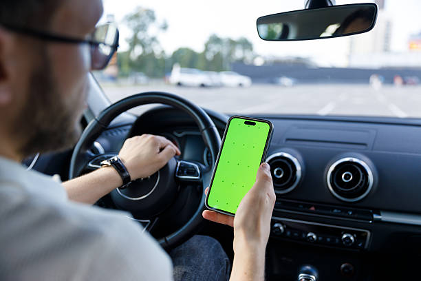 istock A man inside a car using a smartphone with a vibrant green screen, showcasing the intersection of technology and driving in a modern urban setting with clear concentration. 2224693365