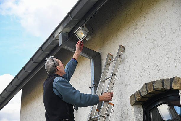 istock Professional electrician installing LED floodlight on ladder, working on house exterior beneath roof gutter, providing enhanced outdoor illumination and security measures 2224693472