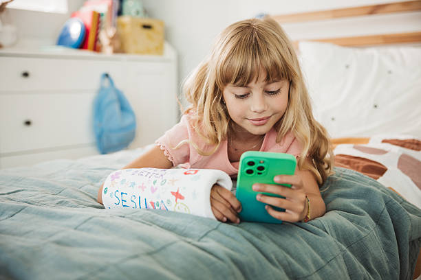 istock Cute girl with a broken arm in orthopedic cast using smartphone 2224693589