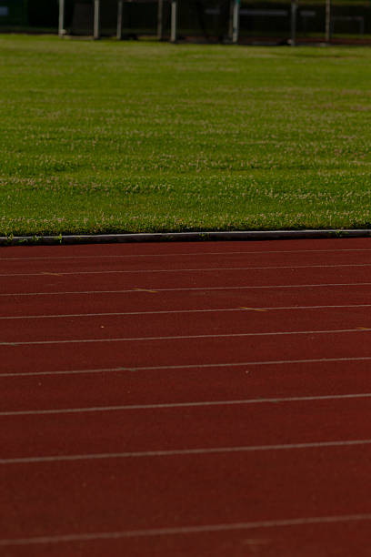 A vibrant red track and field track is prominently displayed with a lush green field in the background, making for a striking sports scene