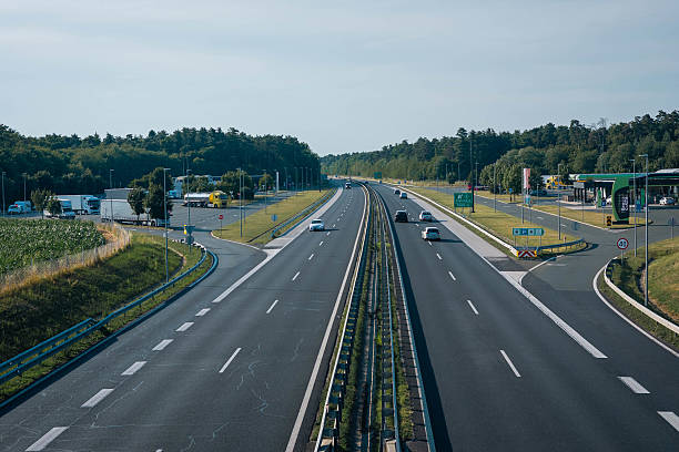 istock clean, modern highway with light traffic, surrounded by green forests and fields. There s a service area with a gas station, trucks, and cars, under a clear blue sky. 2224694583
