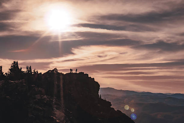 The sun is beginning to set at Grandfather State Park in North Carolina.  There are three silhouetted people on the ridgeline.  There is lens flare. The valley is visible on the right-hand side.