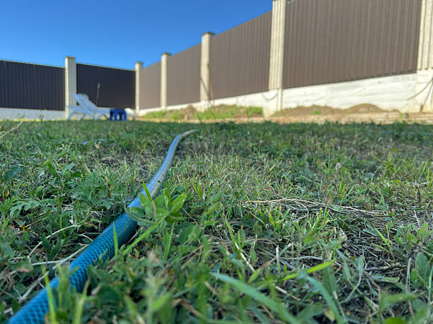 A blue water hose with a knot in it on some very dry looking grass affected by drought.
