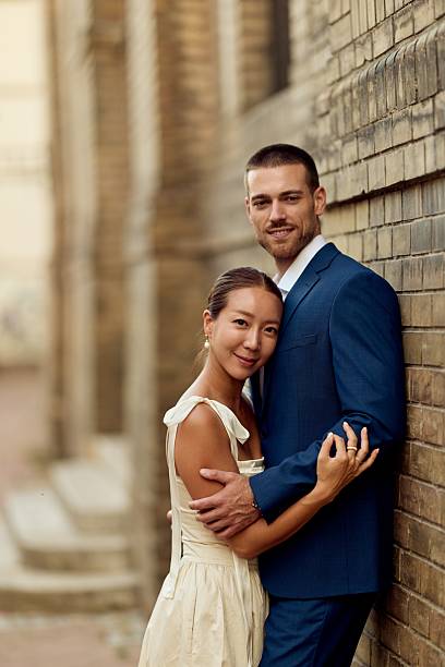Stylish couple embracing against a brick wall, showcasing elegance and affectionate bond.