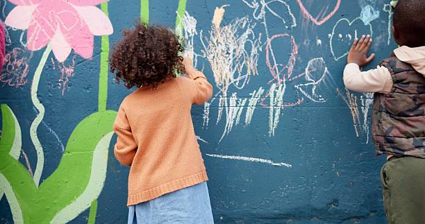 istock Wall, kids and creative with chalk for drawing, cognitive development and education in school. Back, students and children with learning for writing mural, inspiration and outdoor in kindergarten 2224712709