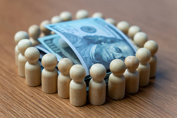 istock A stack of U.S. hundred-dollar bills surrounded by a wooden human figurines. 2224723356