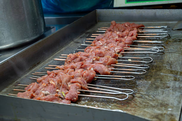 Skewers of kebabs cook over the hot coals of a barbecue grill in a home backyard setting, highlighting a summer culinary tradition.