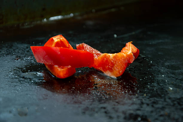 Bright red bell pepper slices are arranged in an artistic manner on a glossy black surface, showcasing culinary creativity during meal preparation.