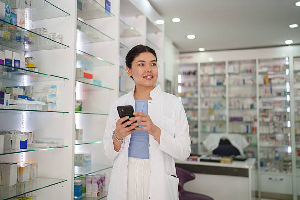 istock Female Pharmacist Using Smartphone Between Medicine Shelves 2224737539