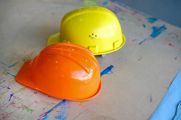 Construction and work site: Two yellow and orange construction helmets lying on a paint-splattered work surface, with selective focus and ample copy space