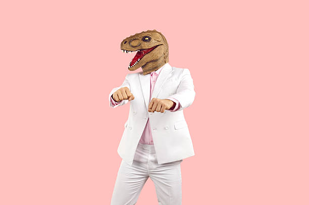 istock Strange guy in suit and funny dinosaur mask dancing against pink studio background 2224746999