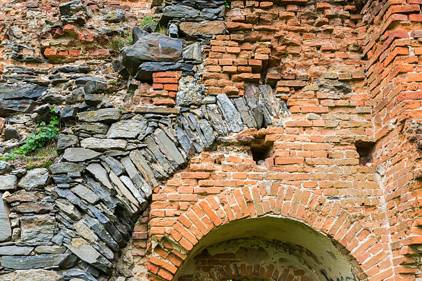 Fragment of the old defense structure built of stones and red bricks in ruined medieval castle in spring overcast day, view from the courtyard side
