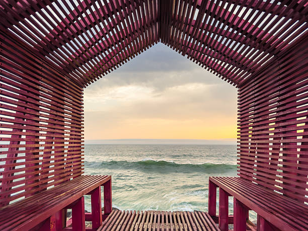 A unique red wooden structure frames the expansive ocean and a pastel sky at sunset over Esmoriz Beach, Ovar, Portugal