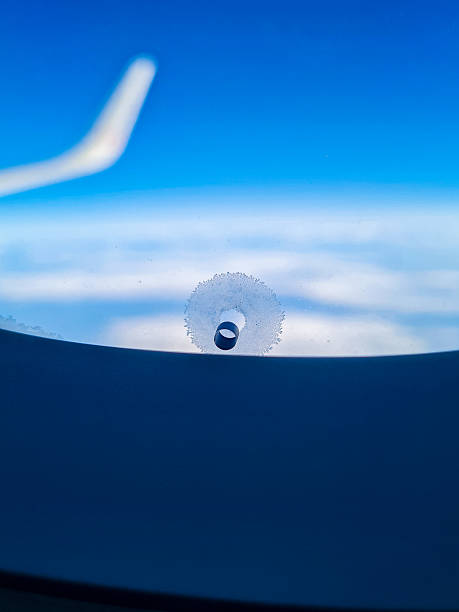 A close-up of a pressure equalization hole with frost forming around it, against a background of an airplane wing, blue sky and clouds. Ideal for travel, aviation, technology or flight themes.