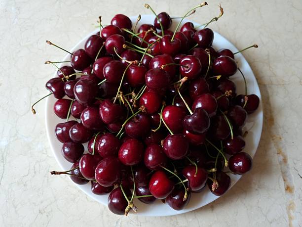 Ripe berries of picked cherries in a white plate on a marble surface