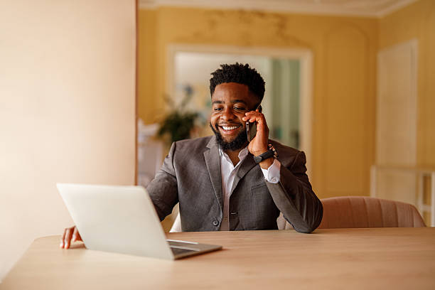 istock Portrait of confident male manager discussing project details over phone call while using laptop at desk 2224764324