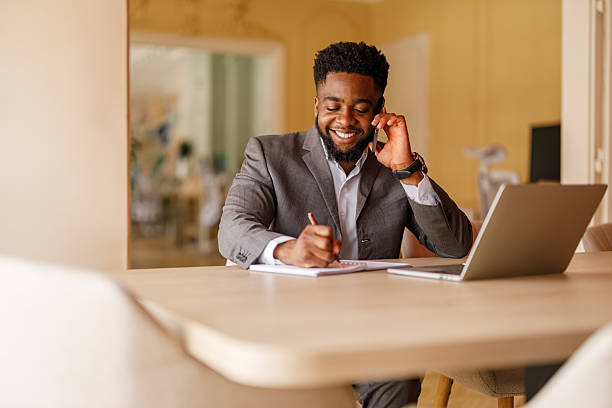 istock Young businessman smiling and taking notes during phone call while working on project at desk in modern office 2224764329