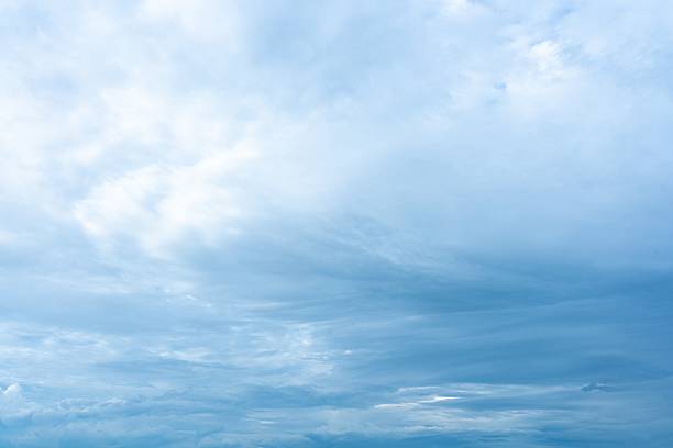 A vast blue sky displays a range of cloud formations from bright soft white clouds to deeper layered grey ones The scene shows varying light conditions and atmospheric depth