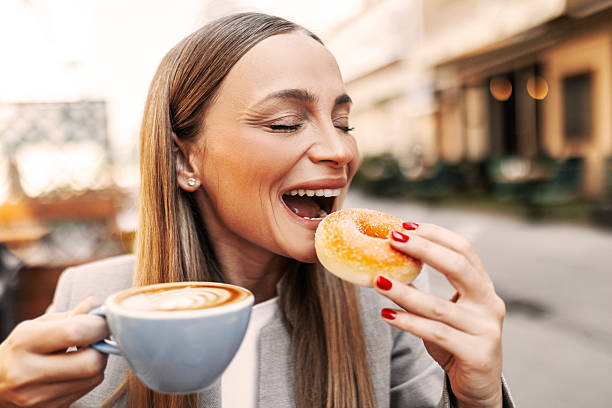 istock Cheerful Woman Sipping Coffee and Eating a Doughnut 2224774070
