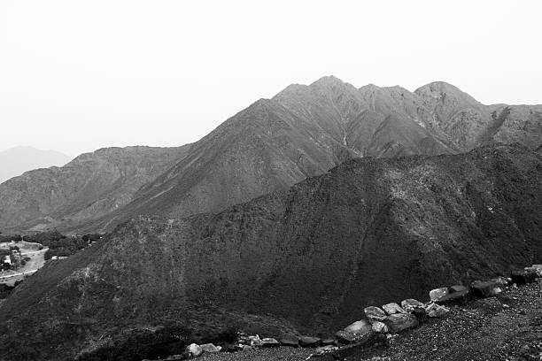 Majestic mountainous landscape in black and white. Rugged terrain with sharp peaks, rocky foreground, and distant valleys under a clear sky