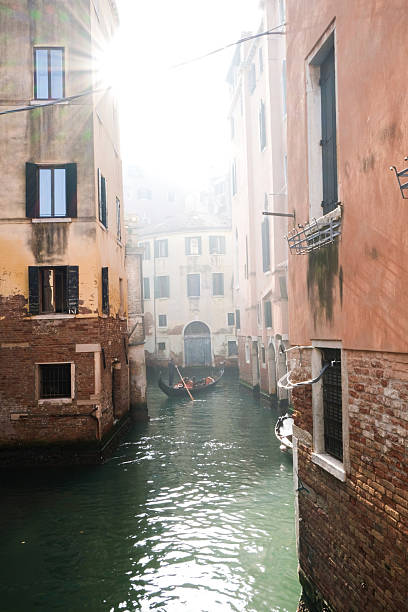 Gondola view in foggy Venice canal, creating a serene atmosphere. Boat silhouette visible, embodying romantic travel. Classic Venice scene in moody weather.