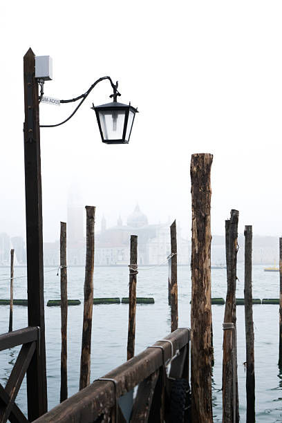Gondola view in foggy Venice canal, creating a serene atmosphere. Boat silhouette visible, embodying romantic travel. Classic Venice scene in moody weather.