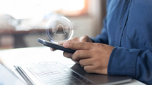 A businessman using a smartphone with a notification bell icon, symbolizing digital alert, mobile notification, reminder, and app communication in modern business.