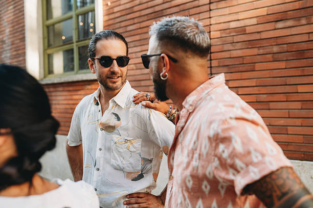 Two mid adult men in casual summer attire engaging in conversation outside a brick building, exuding a relaxed and friendly atmosphere