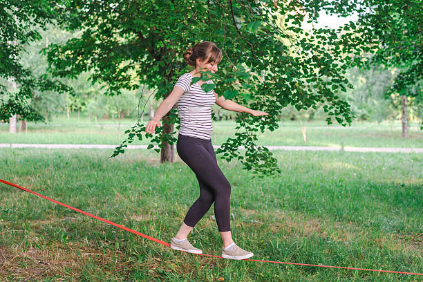 Young woman carefully balancing on a slackline in a green park, enjoying outdoor activity and improving balance
