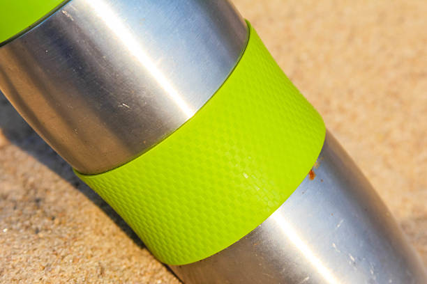 istock Stainless steel thermos bottle with bright green silicone band on sandy surface 2224792466