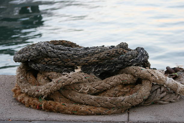 Harbor mooring post, thick ropes around it,  sea water in the background. Burela harbor, Lugo province, Galicia, Spain.