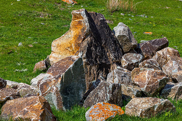 Pile of rocks of various sizes and colors rests peacefully in a grassy field in Kyrgyzstan highlands at summer day.