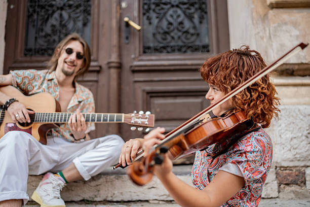 Musical performers playing the guitar and violin on aged outdoor steps beside a weathered building, exuding creativity, joy, and the charm of street music.