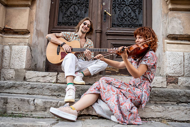 Two musicians collaborate while playing acoustic guitar and violin on historic stone steps, exuding creativity and joy. The image captures a casual yet vibrant scene of outdoor musical expression.