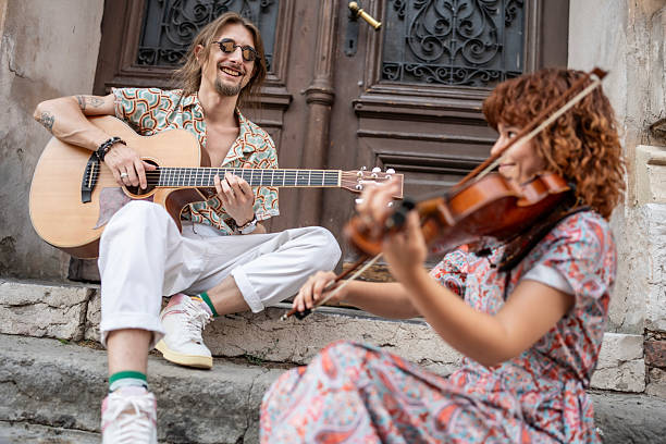 A cheerful moment featuring two musicians collaborating outdoors, playing guitar and violin near an ornate door.
