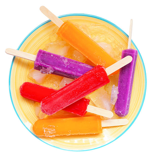 Colorful summer popsicles on a bright yellow plate. Top down view isolated on a white background.