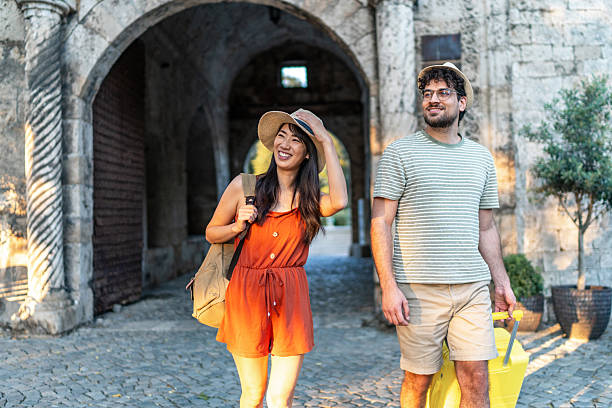 Young multi-ethnic couple of tourists walking through the city, carrying a backpack and suitcase, enjoying their adventure while discovering new places and embracing the vibrant atmosphere