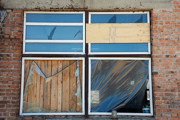Broken and boarded windows showcase the dilapidation of an abandoned structure under bright daylight, highlighting its neglected state