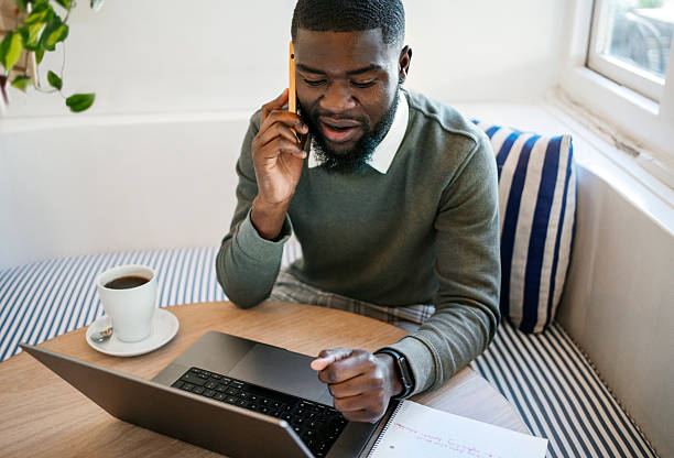 istock Young African man working on laptop and talking on phone in cafe 2224817067