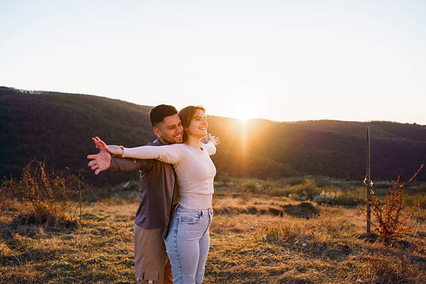 Happy couple stands with arms wide open on a mountain, during sunset.
