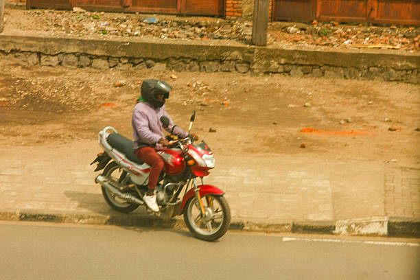 A solo motorcyclist, wearing a helmet, captured on a street in Rubavu, Rwanda. The image shows a common sight of urban transportation in this East African city, highlighting the role of motorcycles in daily commutes and local life. Bathed in warm natural light, this authentic street scene provides a glimpse into the everyday movement within the Rwandan urban environment.