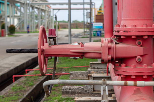 A close up shows a red industrial valve and pipeline system outdoors in daylight, horizontal view.