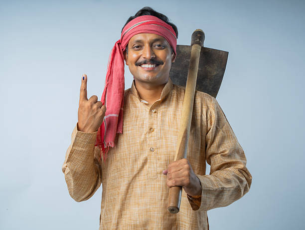 Portrait of smiling mid adult farmer holding shovel and showing index finger with voting ink sign while standing on white background