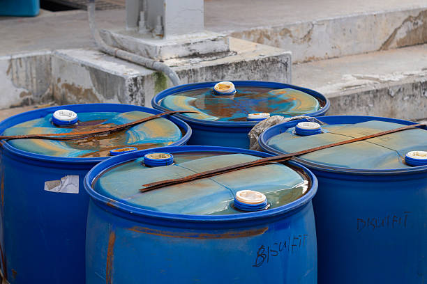 istock Group of Blue Barrels Containing Liquid and Debris, with Rusted Tops and Sticks Over Them 2224855997