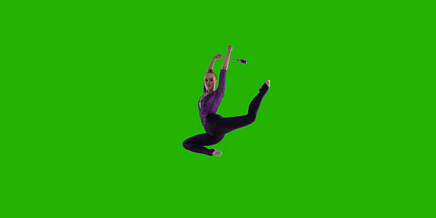 A gymnast girl makes performance with gymnastic band on a large professional stage. She is wearing a professional swimsuit for gymnastics. Behind her is a stadium with spectators.