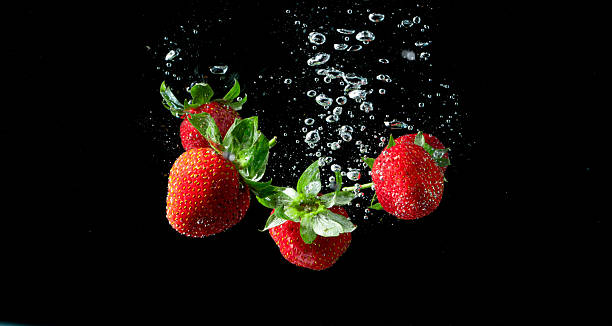 istock Red ripe strawberries falling into water on black background 2224858575