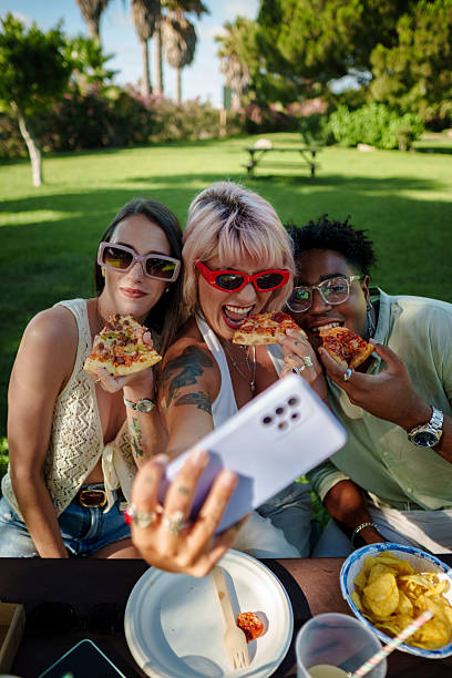 istock Cheerful friends taking a selfie while eating pizza at a picnic 2224860415