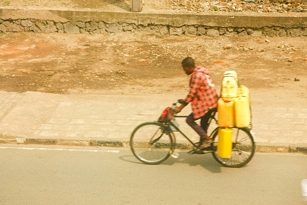 This candid photograph illustrates a man's effort in transporting essential resources in Rubavu, Rwanda. The vibrant yellow jerrycans stand out against the earthy tones of the street and background, highlighting the ingenuity and daily routines of local life. It offers a glimpse into the challenges and solutions for water access in the area.