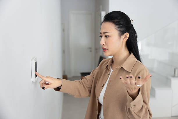 istock Frustrated or concerned woman points at wall-mounted digital thermostat 2224864851